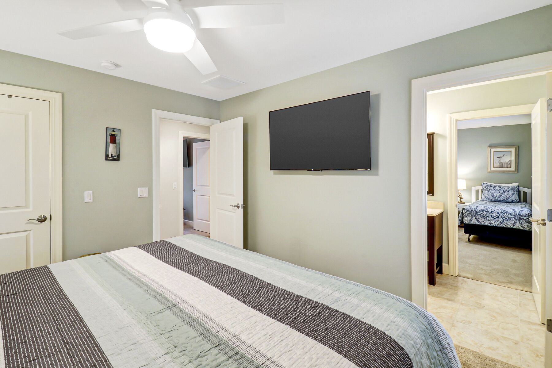 Una camera da letto con un letto, una ventola a soffitto, una TV e una porta che dà su un'altra stanza.