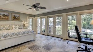 A bedroom with a bed, a ceiling fan, and large windows.