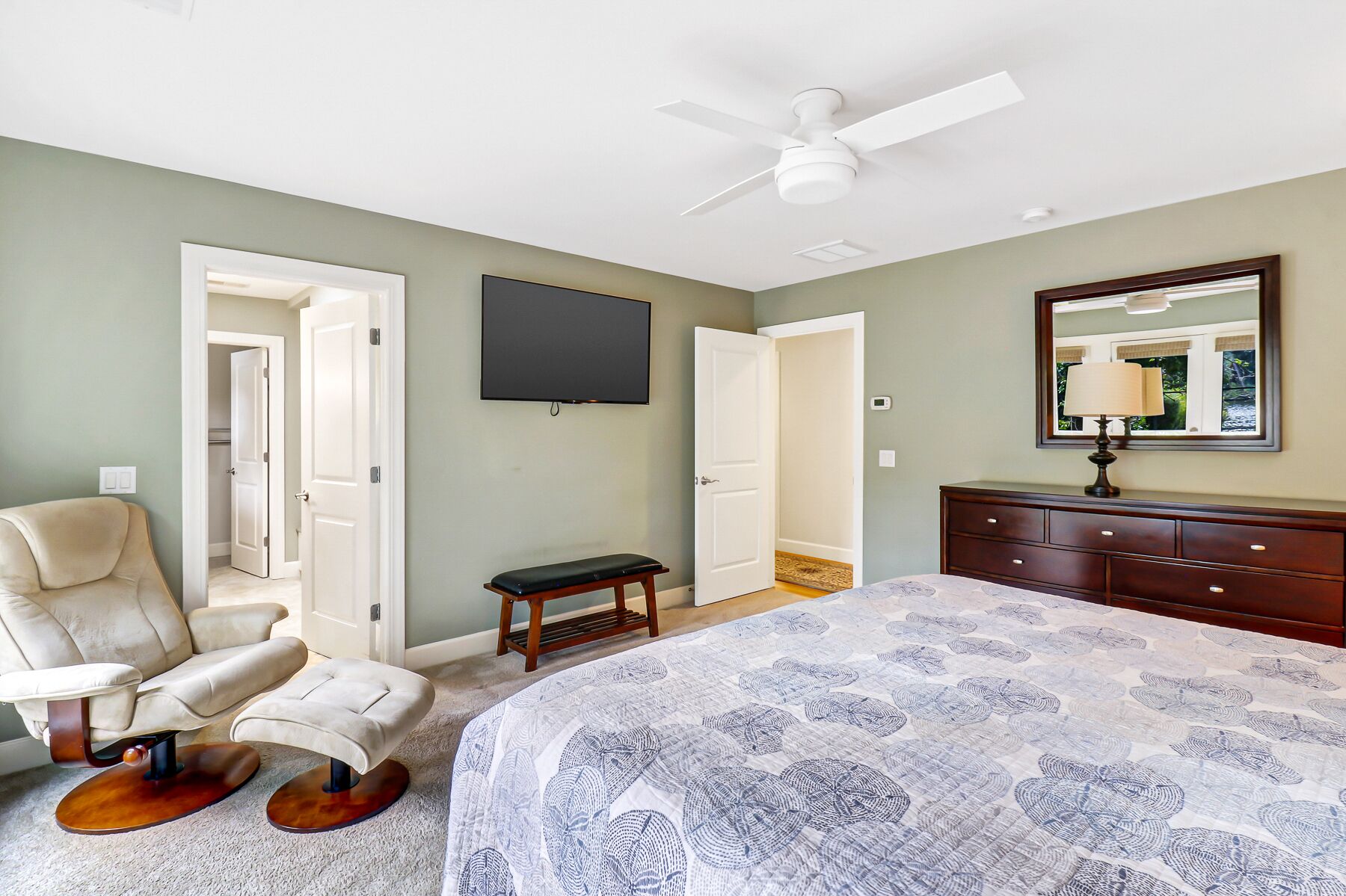 A bedroom with a bed, a chair, a desk, a dresser, a ceiling fan, and a TV.
