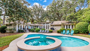 A backyard with a hot tub, a swimming pool, and a patio with chairs.