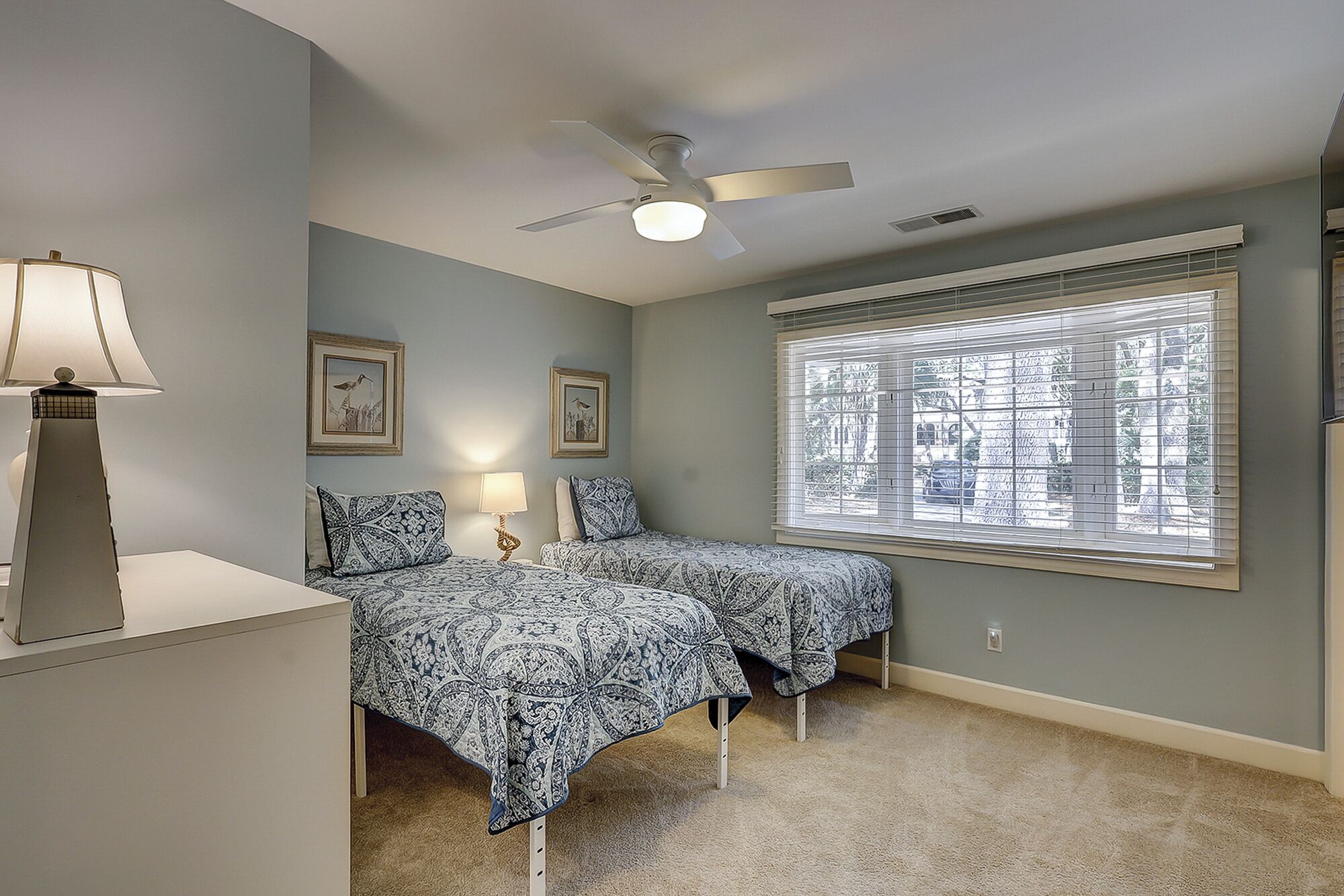 A bedroom with two beds, a ceiling fan, and a window with blinds.