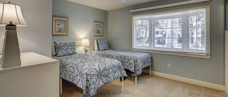A bedroom with two beds, a ceiling fan, and a window with blinds.