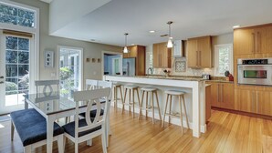 A modern kitchen with wooden cabinets, a central island, bar stools, and a dining table with chairs.