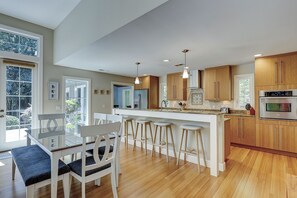 A modern kitchen with wooden cabinets, a central island, bar stools, and a dining table with chairs.
