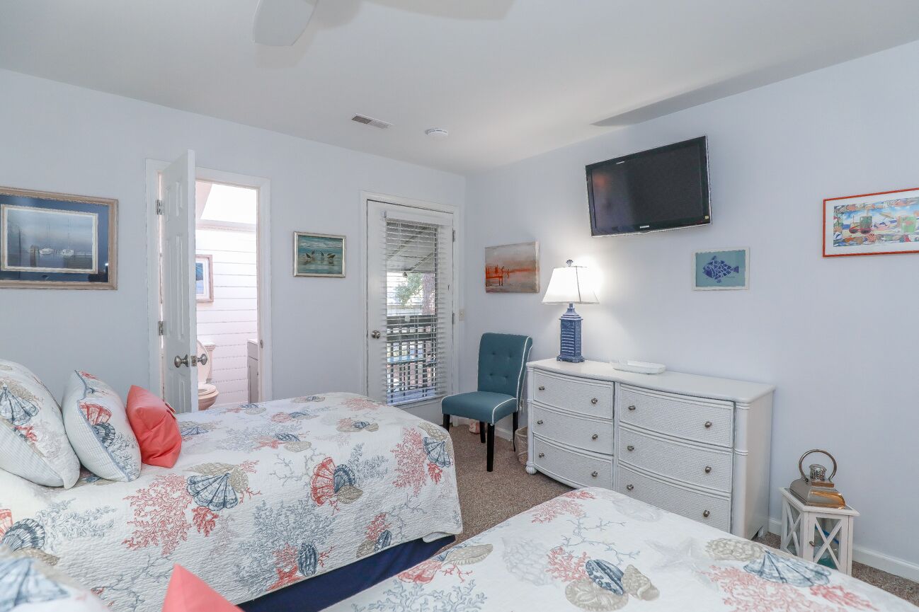 Ein Schlafzimmer mit einem Bett, einem Schminktisch, einem Sessel und einem Fernseher an der Wand.