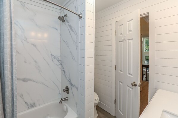 A bathroom with a marble shower and a white door leading to another room.