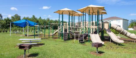 A playground with slides and climbing structures, picnic tables, and umbrellas.