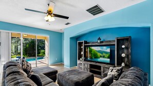 A living room with a large flat-screen TV, dark grey sofas, and a ceiling fan. - Aster Cove (Kissimmee)