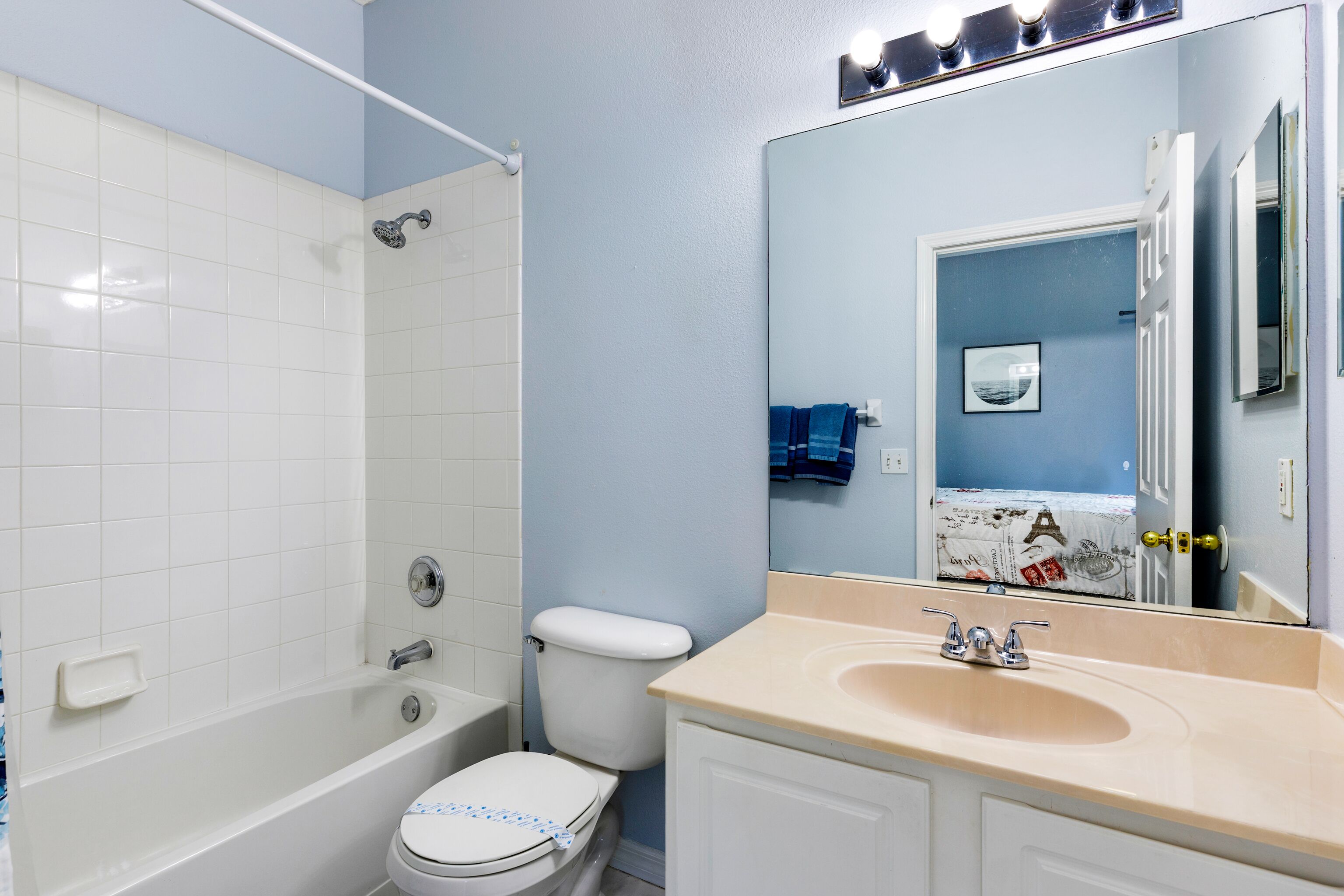 A bathroom with a bathtub, toilet, sink, and a mirror reflecting a door and a towel rack.