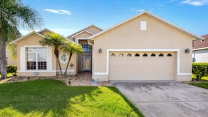 A single-story house with a beige exterior, a front garage, and a well-maintained lawn. - Aster Cove (Kissimmee)