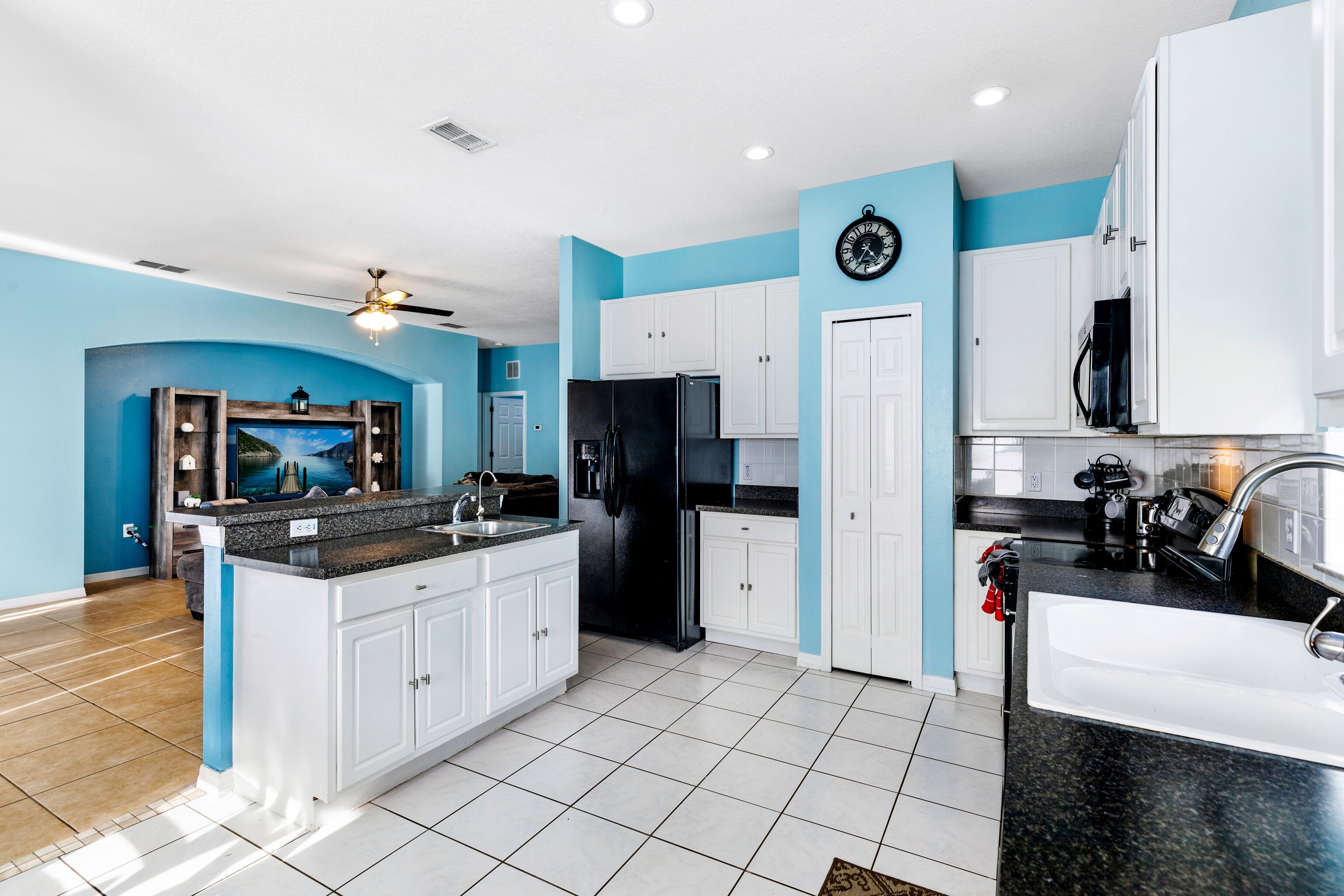 Une cuisine moderne avec des meubles blancs, un réfrigérateur noir et un mur d’accent bleu.