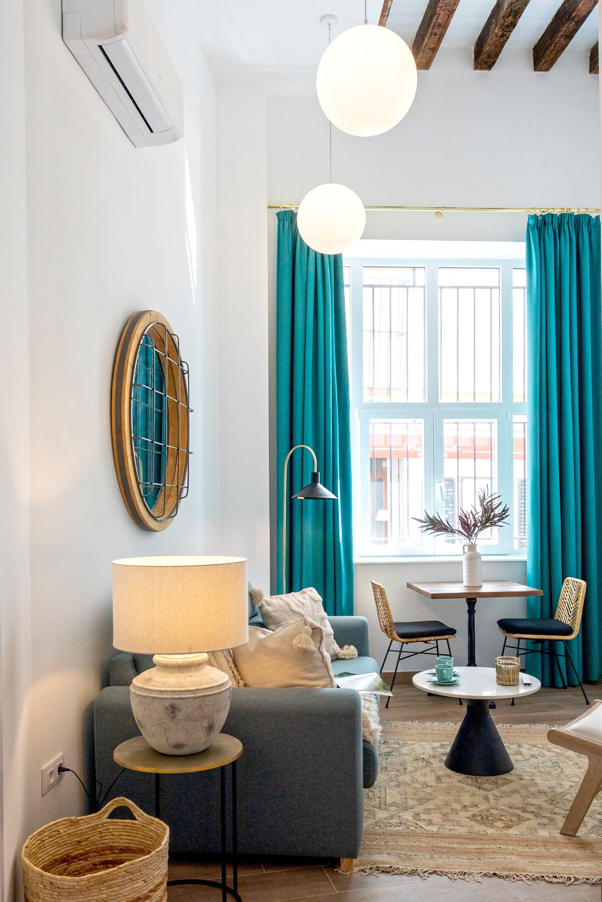 Ein modernes Wohnzimmer mit grauem Sofa, rundem Tisch, blaustichigen Vorhängen und einem großen Fenster.