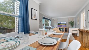 A dining area with a wooden table set for four, white chairs, and a view of the outdoors through large windows. - Theater - Firepit & BBQ - Life Size Games (Minneapolis)