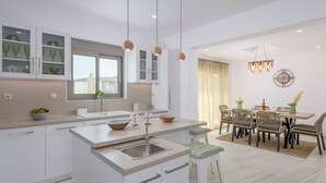 Een moderne keuken met witte kasten, een centraal eiland met een spoelbak en hangende lampen.