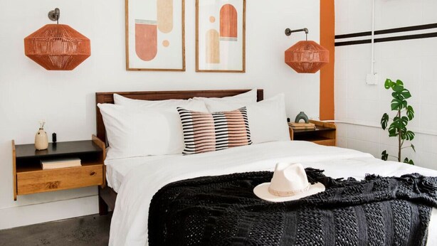 A neatly arranged bedroom with a wooden headboard, a black and white striped pillow, and a white hat on the bed. - Midtown Jewel – Walk Ponce City Market & BeltLine (Atlanta)