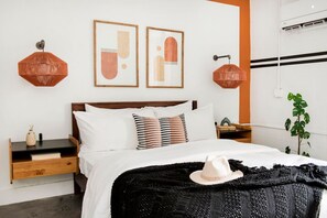 A neatly arranged bedroom with a wooden headboard, a black and white striped pillow, and a white hat on the bed. - Midtown Jewel – Walk Ponce City Market & BeltLine (Atlanta)