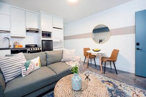 A compact living space with a kitchenette, a grey sofa with striped pillows, a round coffee table, and a blue door.