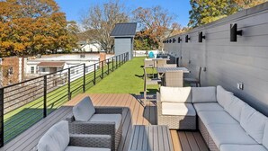 A rooftop patio with outdoor furniture, a small table, and a view of a residential area. - The Layla – Walkable Downtown Apartment + Rooftop (Atlanta)