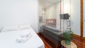 Ett modernt hotellrum med en säng, en soffa, en tv som är monterad på väggen och ett litet bord med en växt.