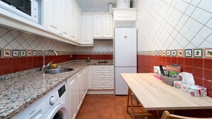 Ett kompakt kök med vita skåp, en bänkskiva i granit, en tvättmaskin, ett kylskåp och ett kakelbeklätt stänkskydd med fruktmotiv.