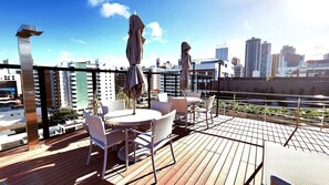 A rooftop terrace with a city view, featuring a table and chairs, umbrellas, and a railing. - Urban by Hosppedar (João Pessoa)