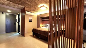 A bedroom with a bed, bedside table, lamp, and a view through a wooden partition. - Urban by Hosppedar (João Pessoa)