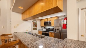 Una cocina con encimeras de granito, armarios de madera y electrodomésticos de acero inoxidable, además de un extintor.