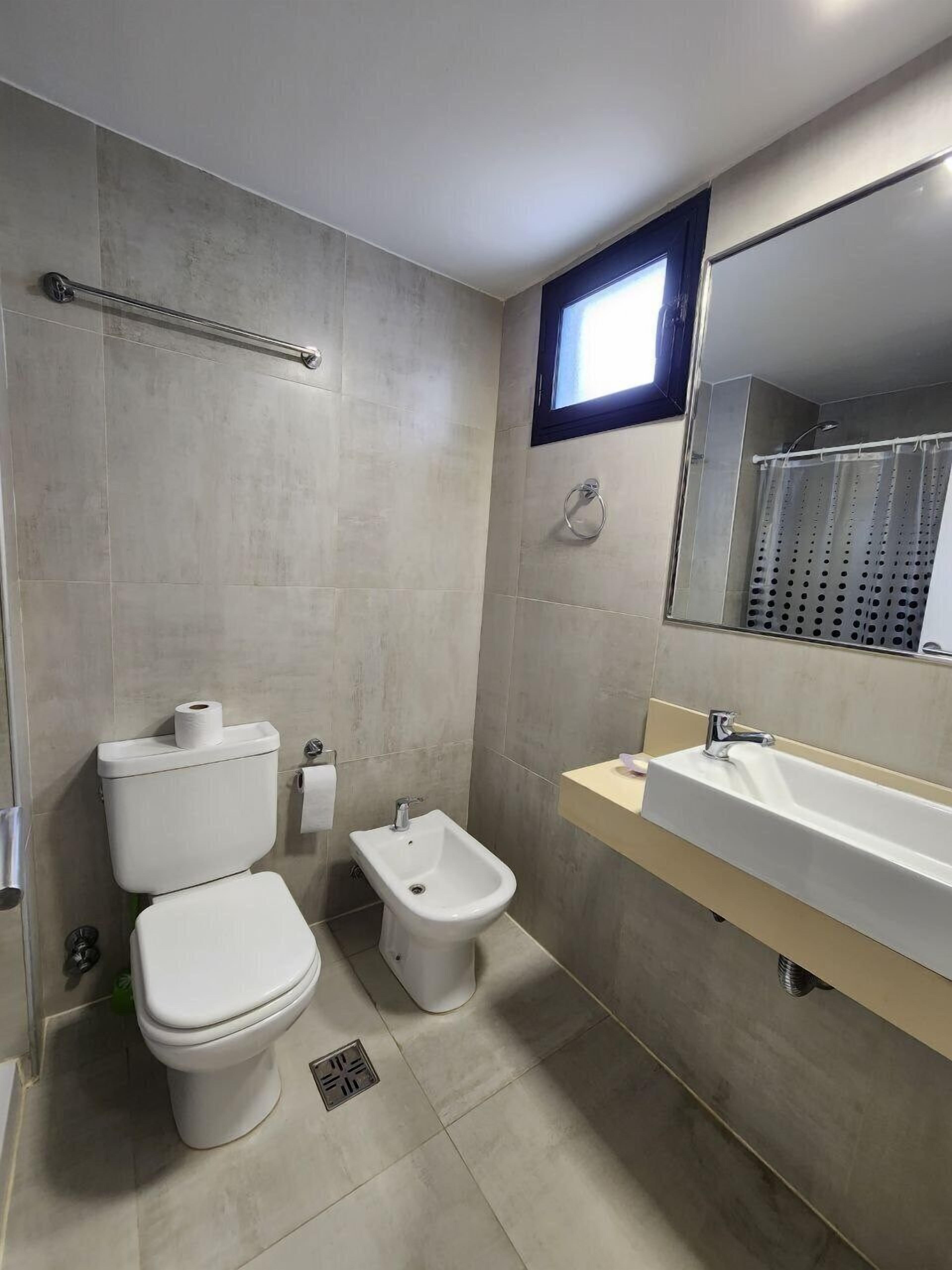 A modern bathroom with a toilet, bidet, and a large sink with a mirror.