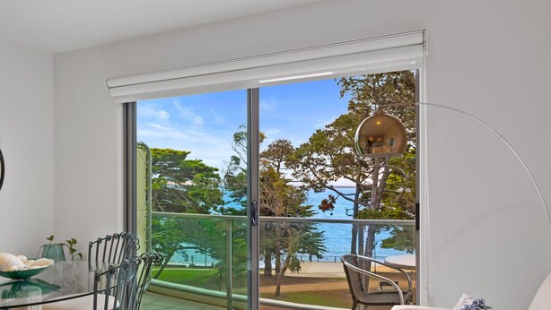 Ein modernes Wohnzimmer mit einer großen Schiebeglastür, die auf einen Balkon mit Blick auf das Meer und Bäume führt.