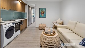 Eine moderne Küche mit integrierten Geräten, eine Essecke mit einer Couch und einem Couchtisch sowie ein Wohnzimmer mit einer Couch und einem Bild an der Wand.