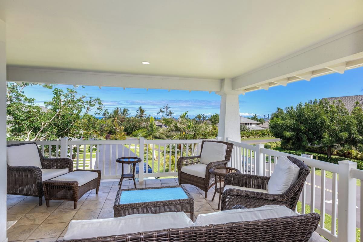 A covered outdoor seating area with wicker furniture and a view of the ocean.
