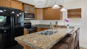 Eine Küche mit Granitarbeitsplatten, Edelstahlgeräten, Holzschränken und einer integrierten Kücheninsel mit Spüle.