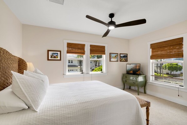 Une chambre à coucher avec un lit, un ventilateur de plafond, une commode et des fenêtres équipées de stores.