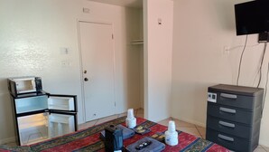 A hotel room with a bed, a small desk with a microwave, a dresser, and a TV mounted on the wall.