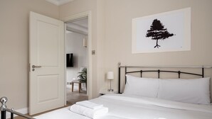 A hotel room with a bed, a bedside table, a lamp, and a wall-mounted artwork of a tree. - GuestReady - Charming residence in Fulham (London)