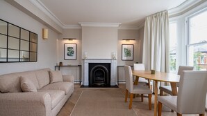 A living room with a fireplace, a sofa, a dining table with chairs, and artwork on the walls. - GuestReady - Charming residence in Fulham (London)