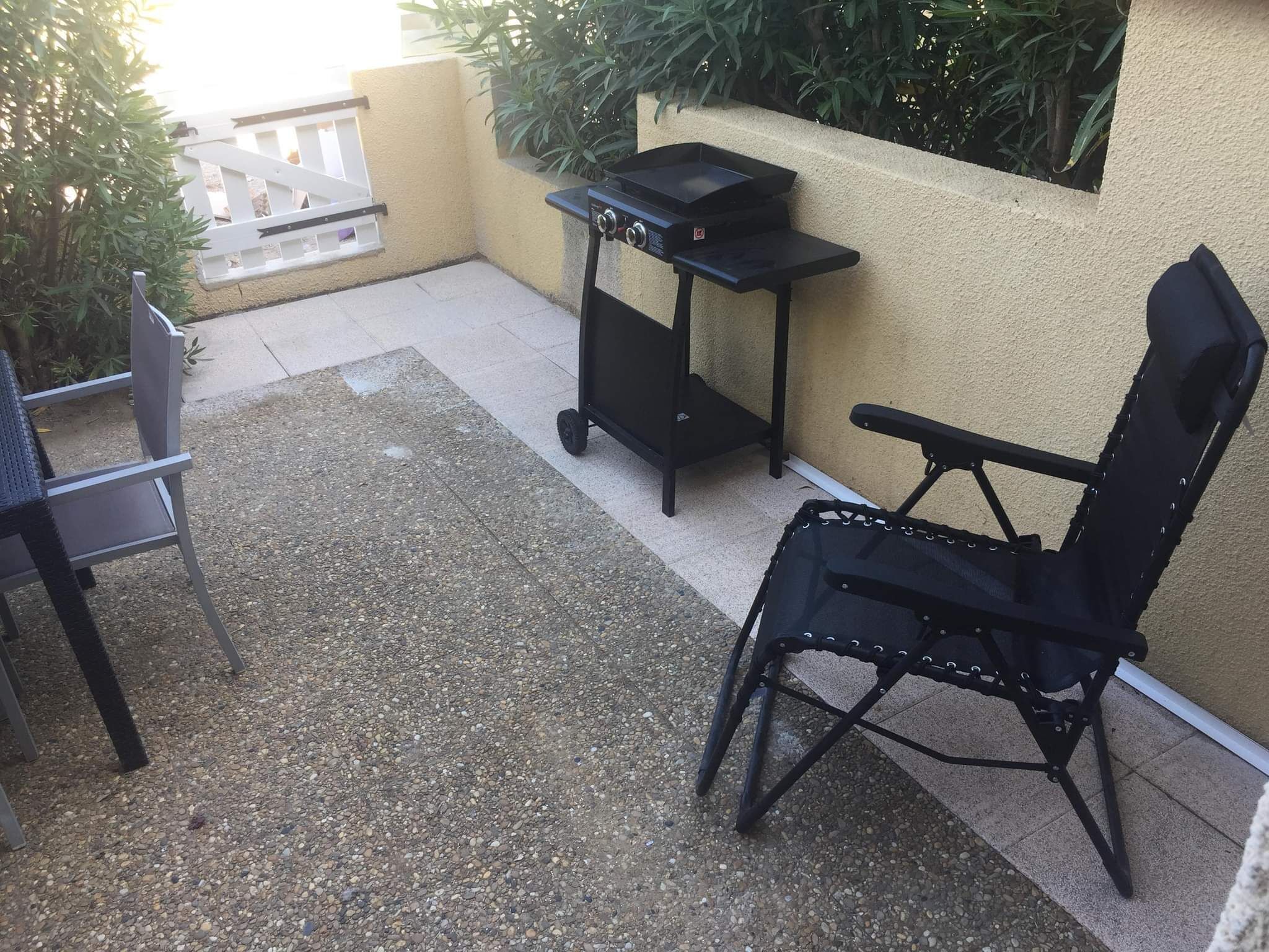 An outdoor patio with a grill, a folding table, and a chair.