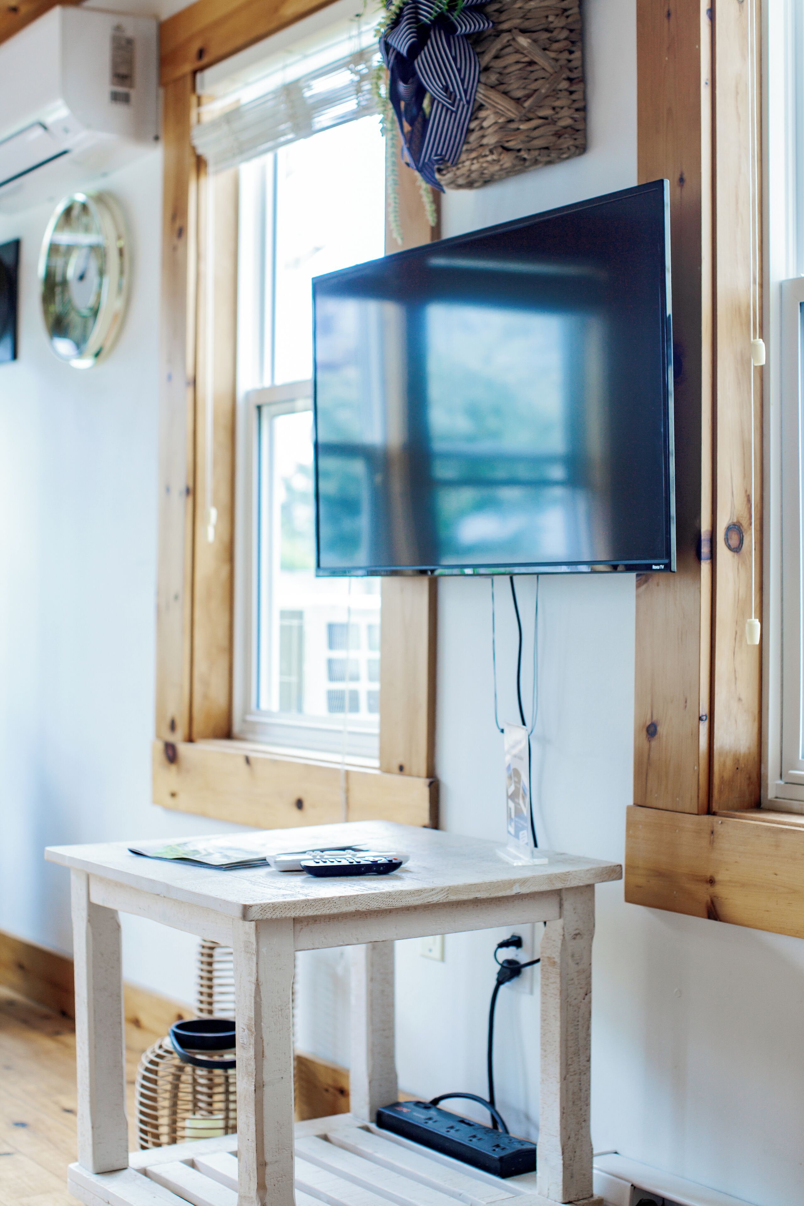 Une pièce équipée d’un téléviseur à écran plat fixé au mur, d’une petite table en bois avec une télécommande, et d’une multiprise posée sur le sol.