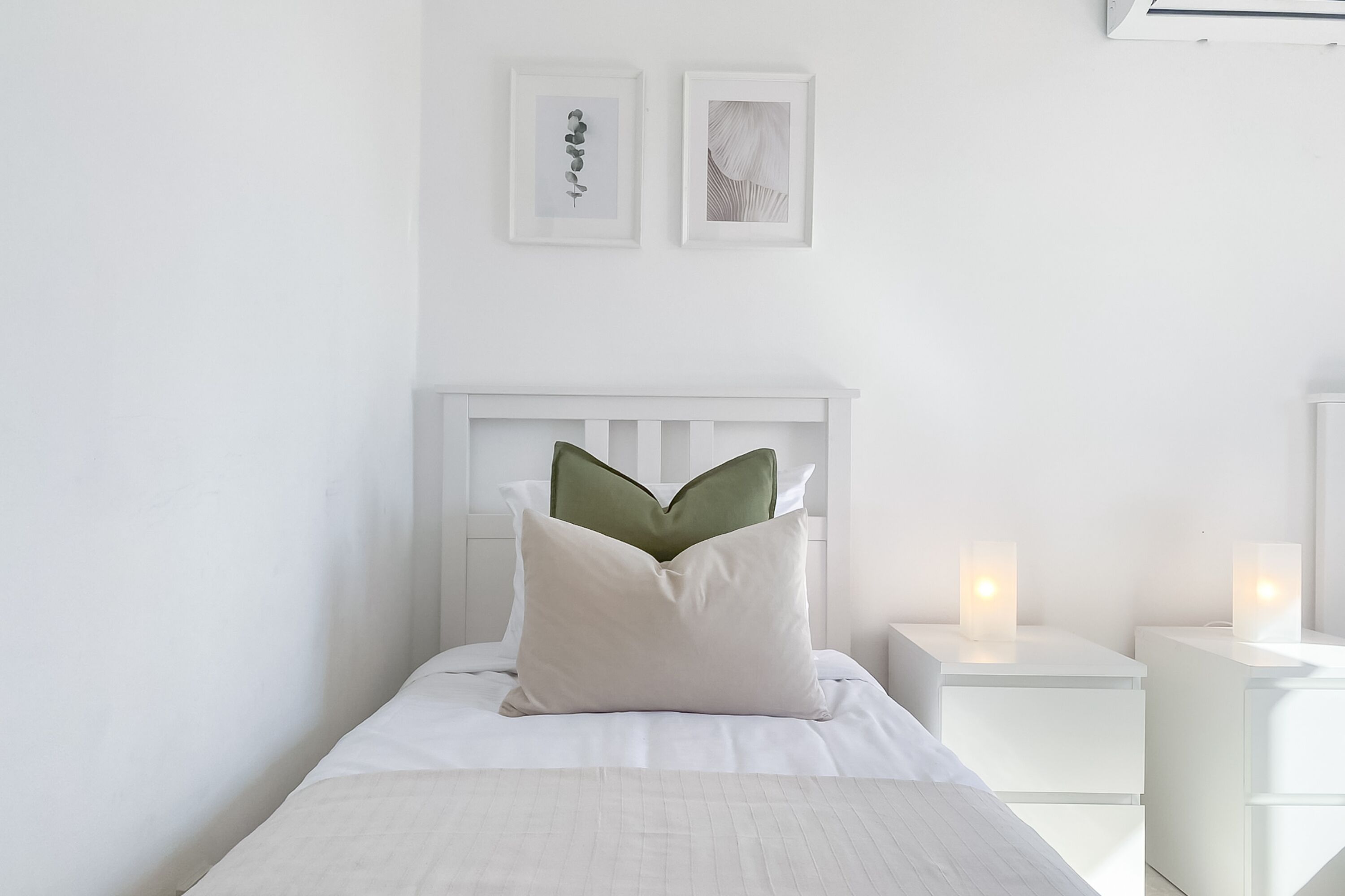 A neatly made bed with a white headboard, a green pillow, and two bedside tables with candles.