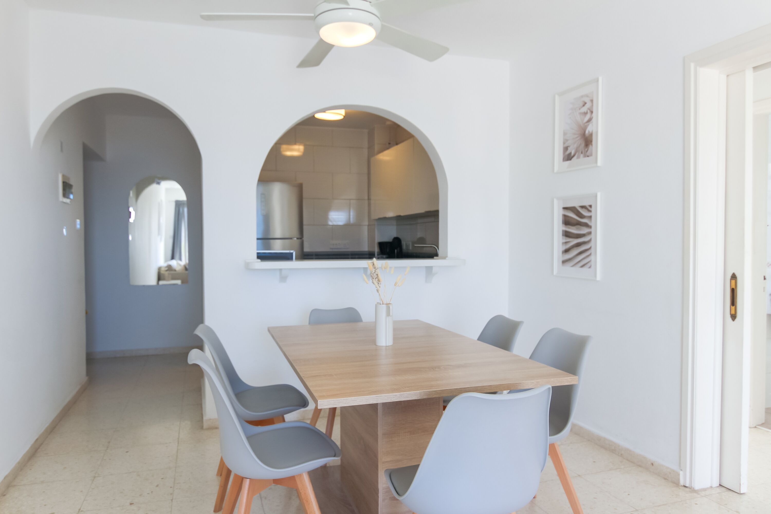 Un comedor con una mesa de madera y sillas grises, un ventanal en arco y un ventilador de techo.