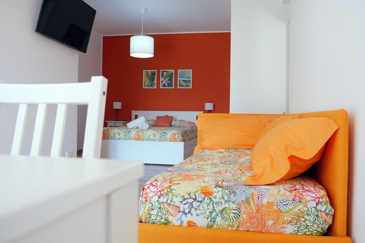 A bedroom with two beds, a TV mounted on the wall, and a white chair.