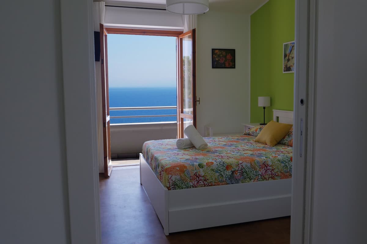 A bedroom with a bed, a view of the sea, and a green wall.