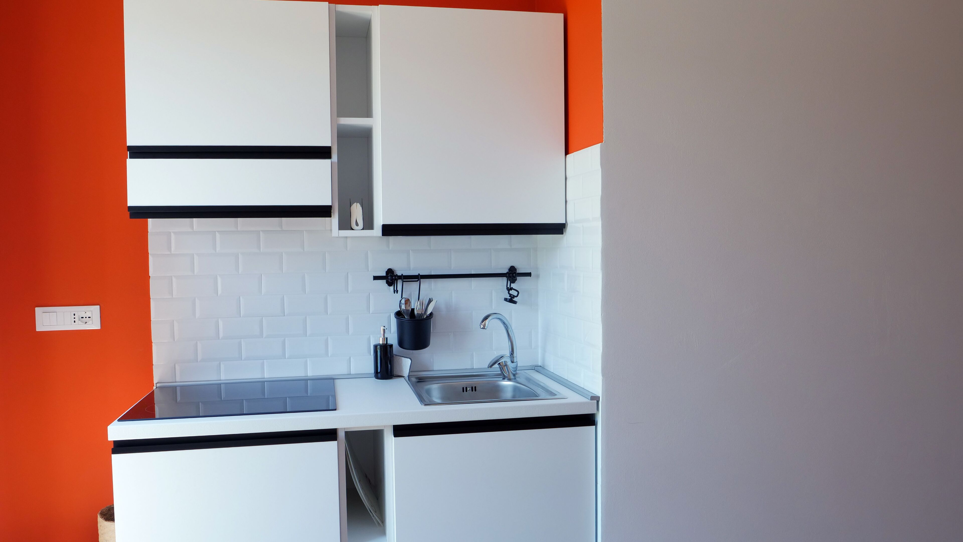 A compact kitchen with white cabinets, a black countertop, and a white brick backsplash.