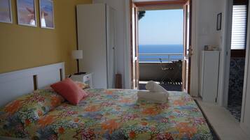 Un dormitorio con cama, mesita de noche, lámpara, ventana con vista al mar y balcón con silla y mesa.