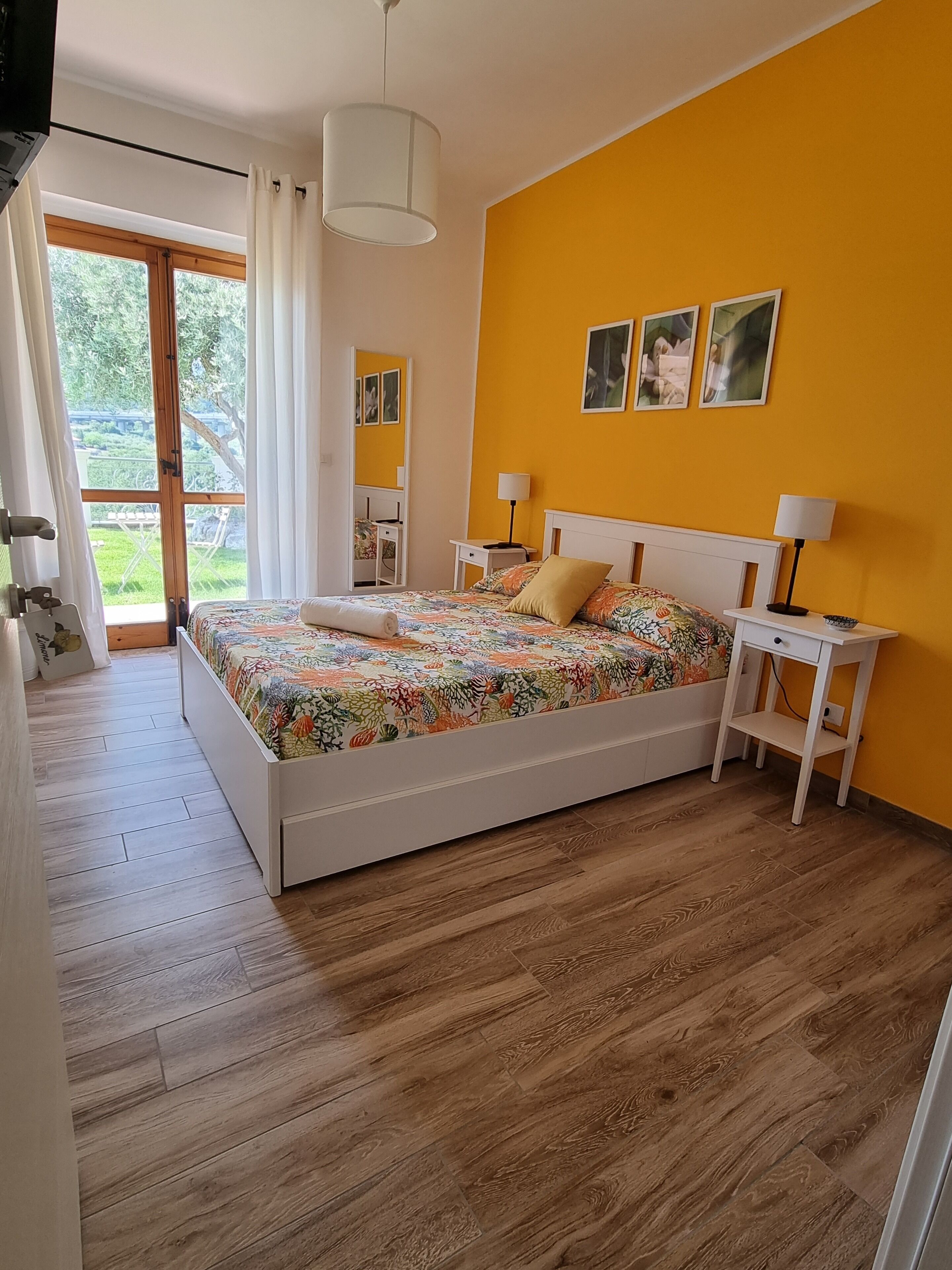 A bedroom with a bed, bedside tables, a window with curtains, and a view of greenery outside.