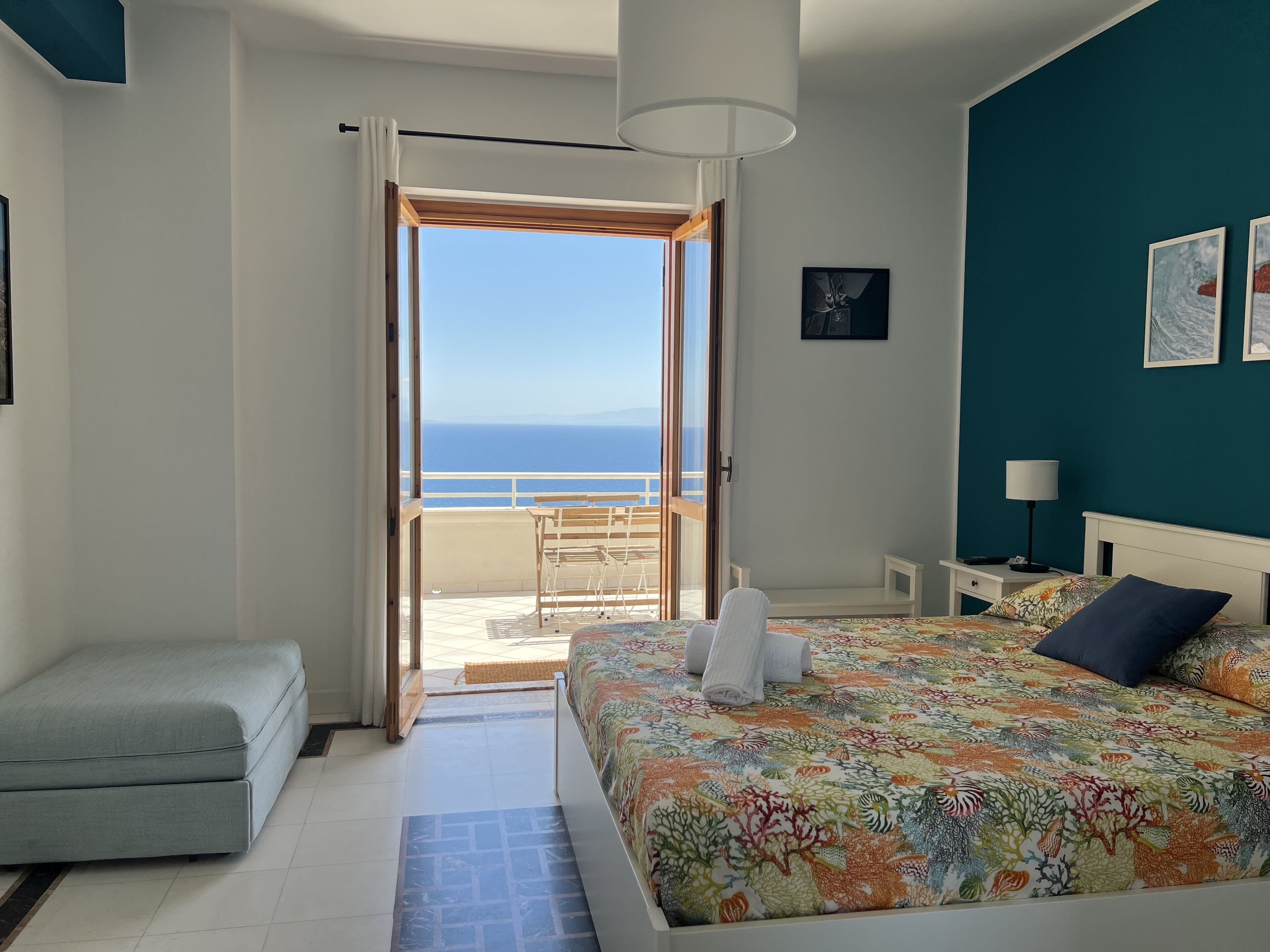 Een slaapkamer met een bed, een zithoekje, een nachtkastje en uitzicht op zee.