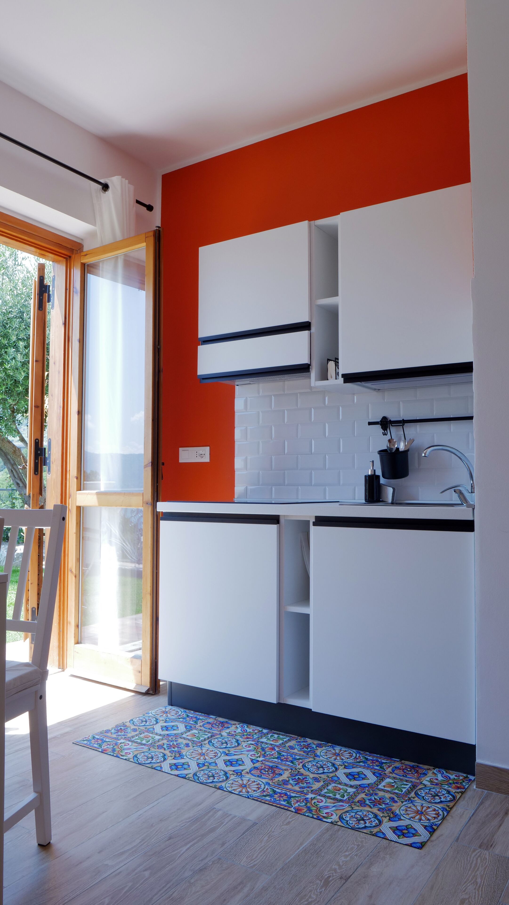 A modern kitchen with white cabinets, a black countertop, and a red accent wall.