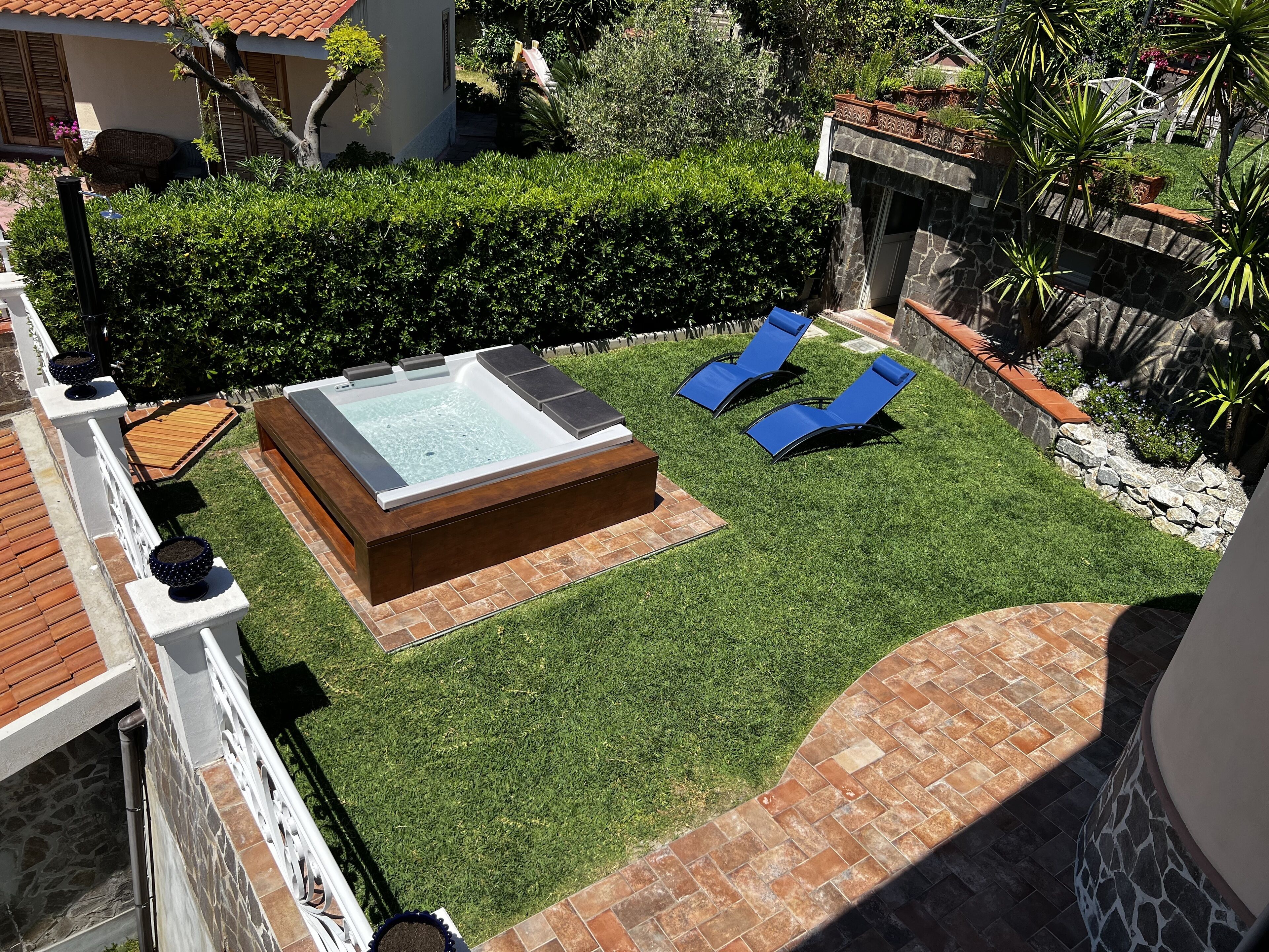 A backyard with a hot tub, two lounge chairs, and a well-maintained lawn.
