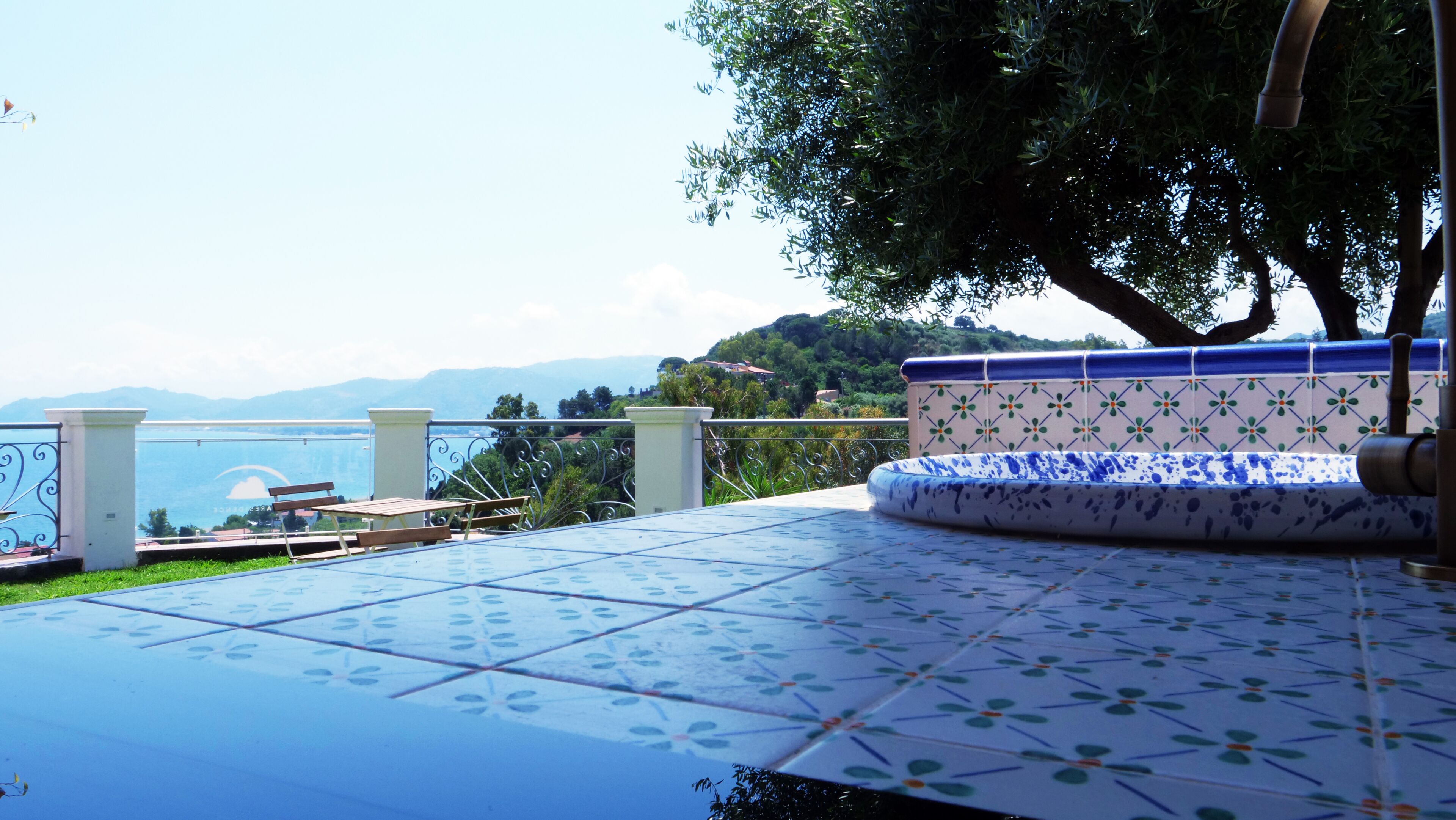 Una terraza con mesa y sillas de diseño, con vistas a un paisaje que incluye una masa de agua y colinas.