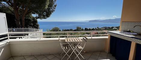 A balcony with a view of the sea, a white fence, and a tiled floor.